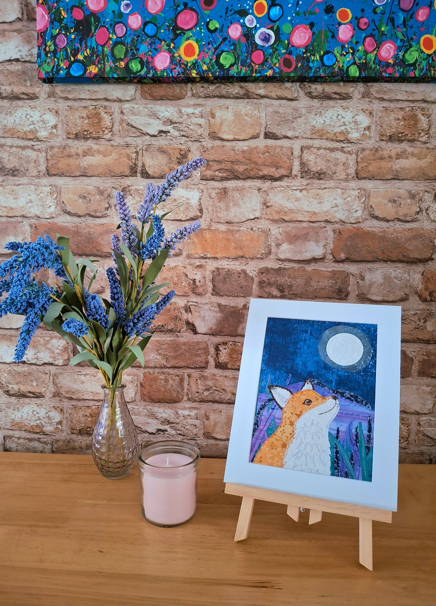 Artistic depiction of a fox in a night scene with a vase of flowers and a candle on a wooden surface against a brick wall.