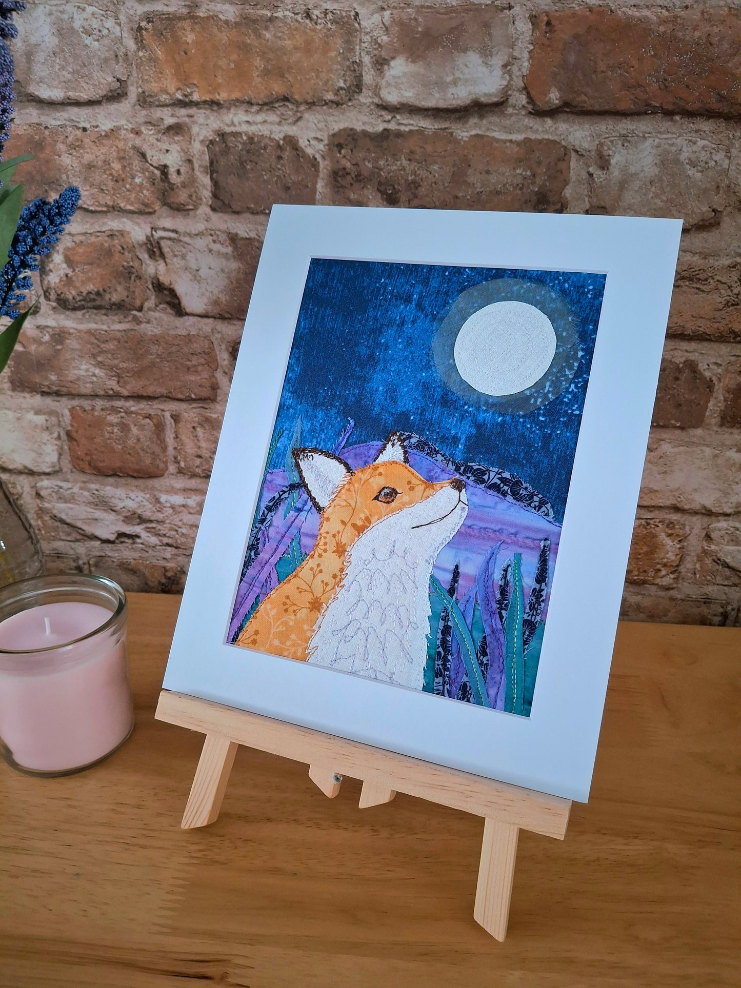Mounted artwork of a fox under a moonlit sky on a wooden surface with a brick wall background.
